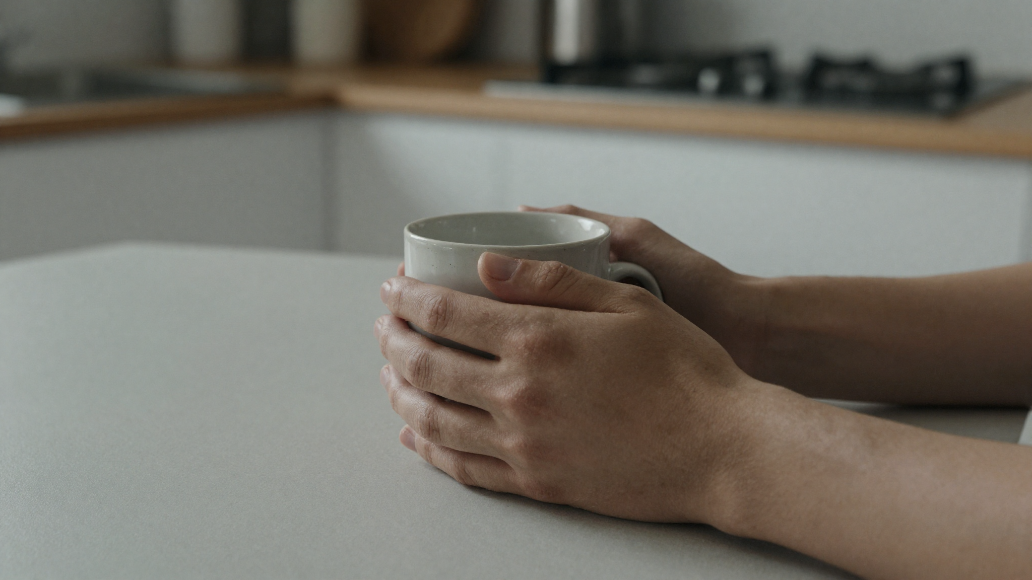 Close-up of a parent hands wrapped around a warm mug at a kitchen table