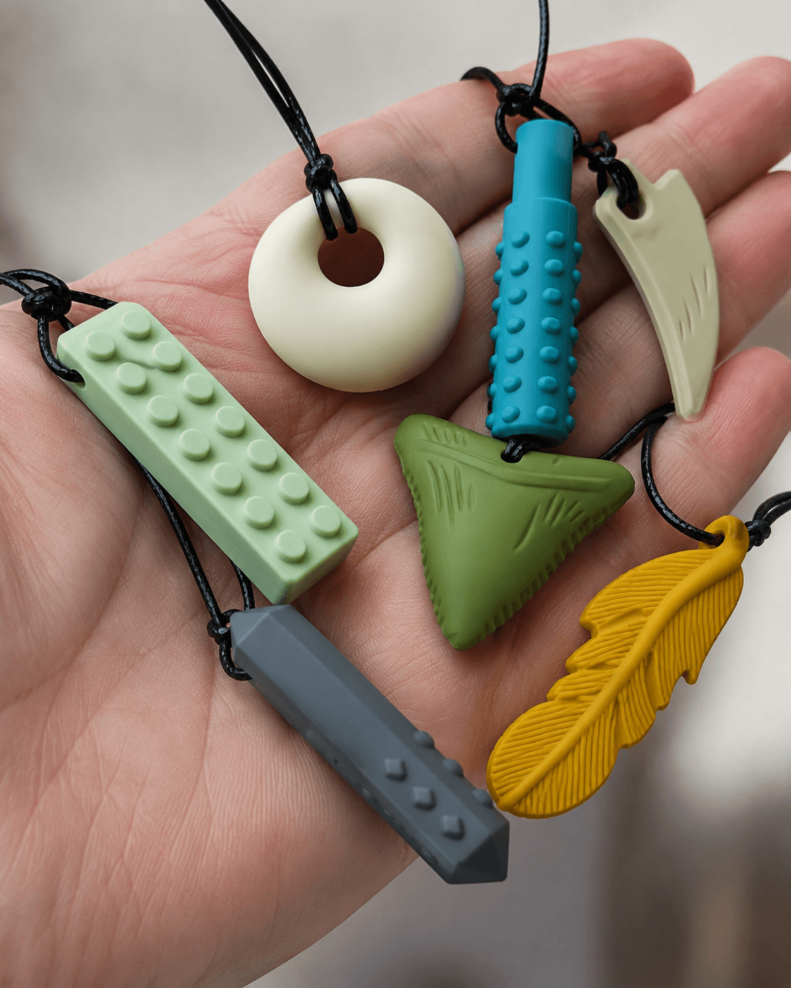 Close-up of several colourful silicone chew necklace pendants of different shapes held in a hand