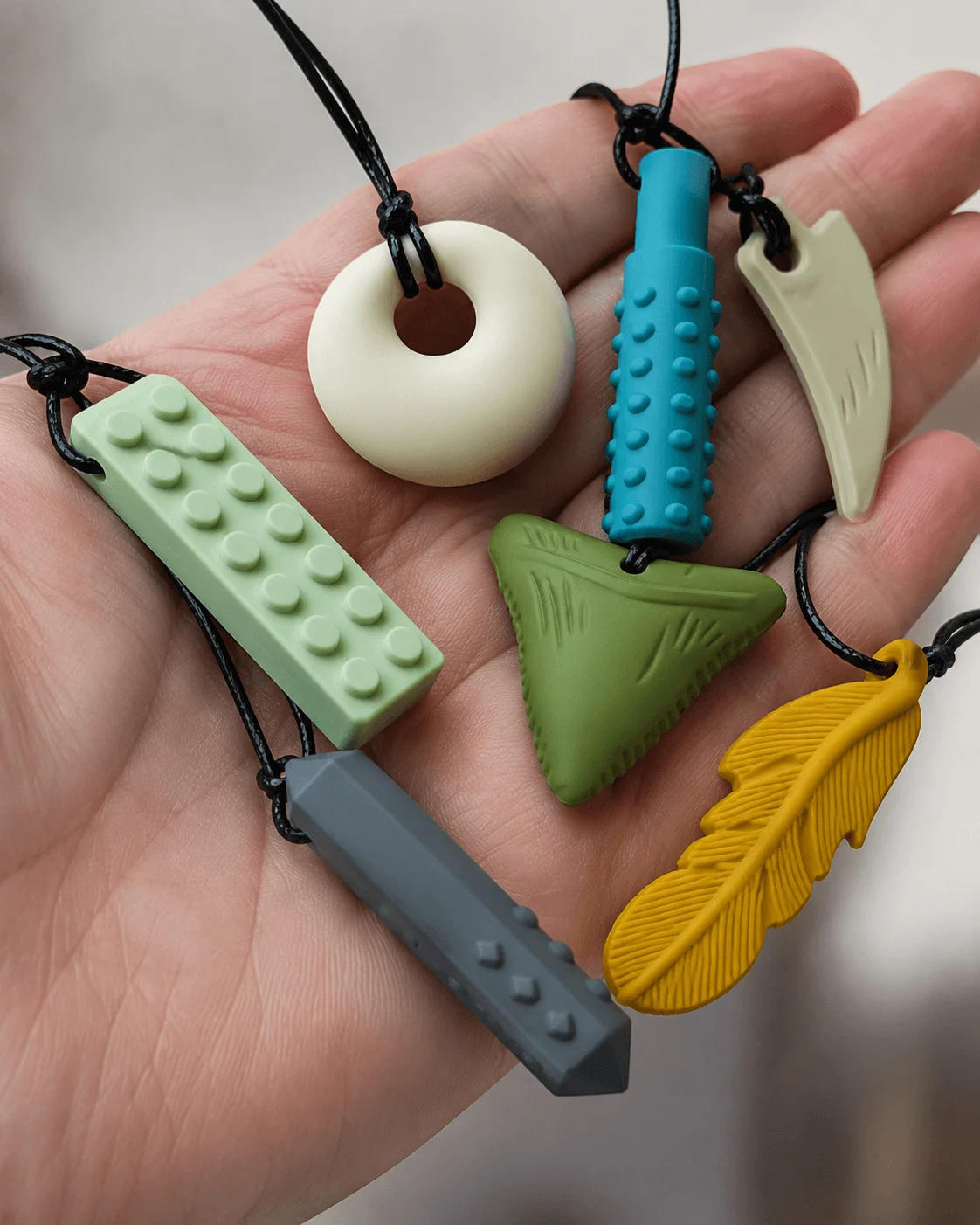 Close-up of several colourful silicone chew necklace pendants of different shapes held in a hand