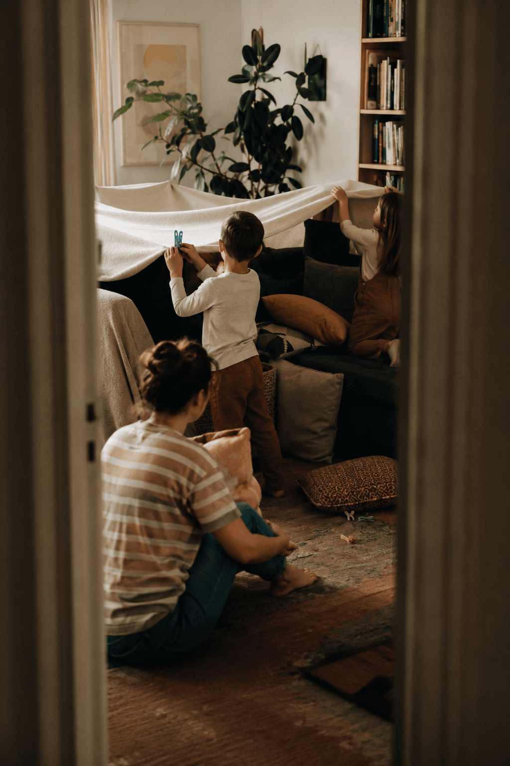 Two children build a blanket fort together in the living room, fully absorbed in the project