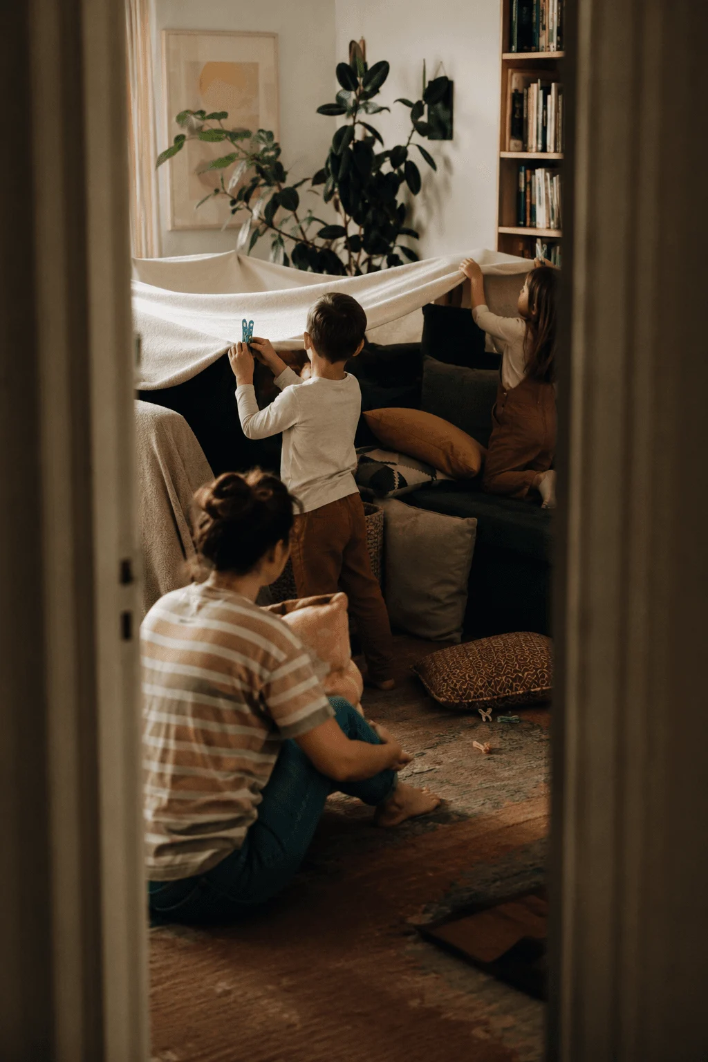 Two children build a blanket fort together in the living room, fully absorbed in the project