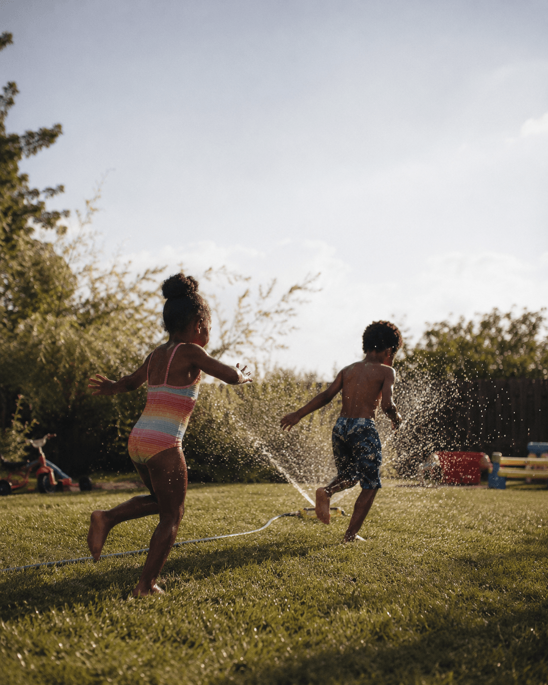 Two children play together in a sprinkler in a backyard on a summer day