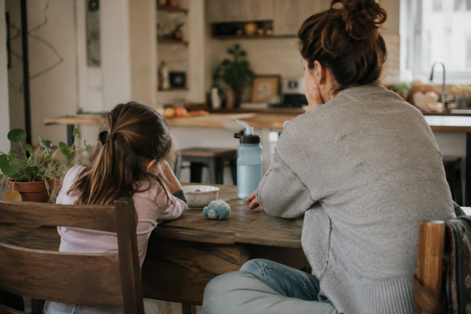 Mother and daughter packing a school bag at the breakfast table with a quiet fidget nearby