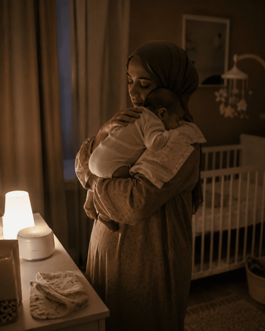 Mother holds her baby in a dim nursery at night beside the crib and a small glowing nightlight