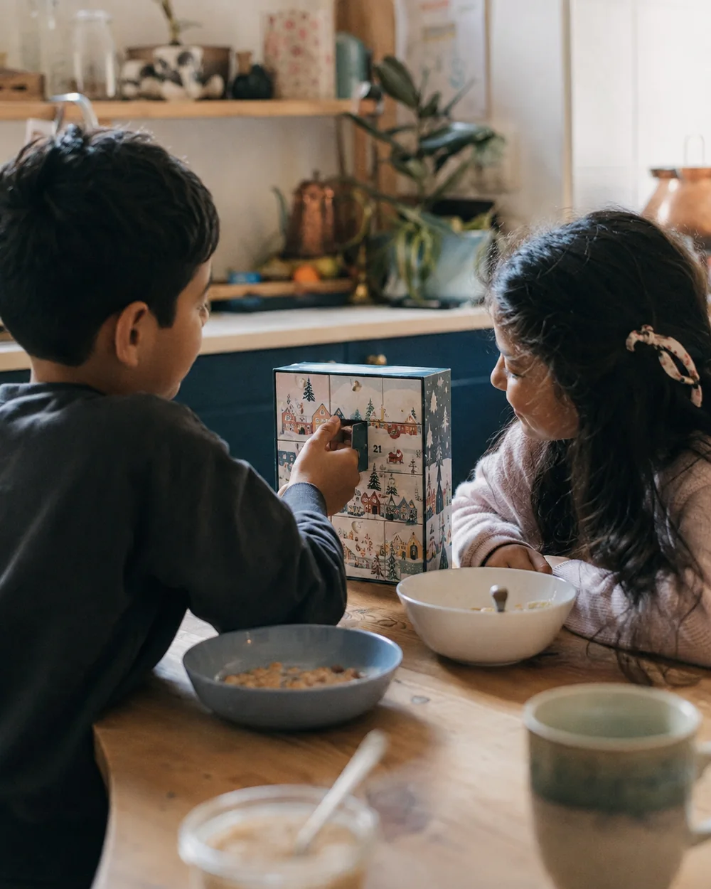 A boy and a girl at the breakfast table opening drawer twenty one of a wooden advent calendar
