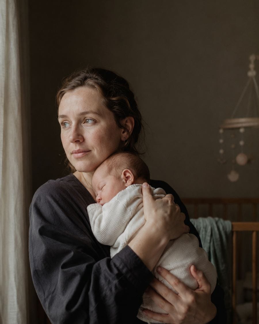 A mother stands in a nursery holding her newborn against her chest