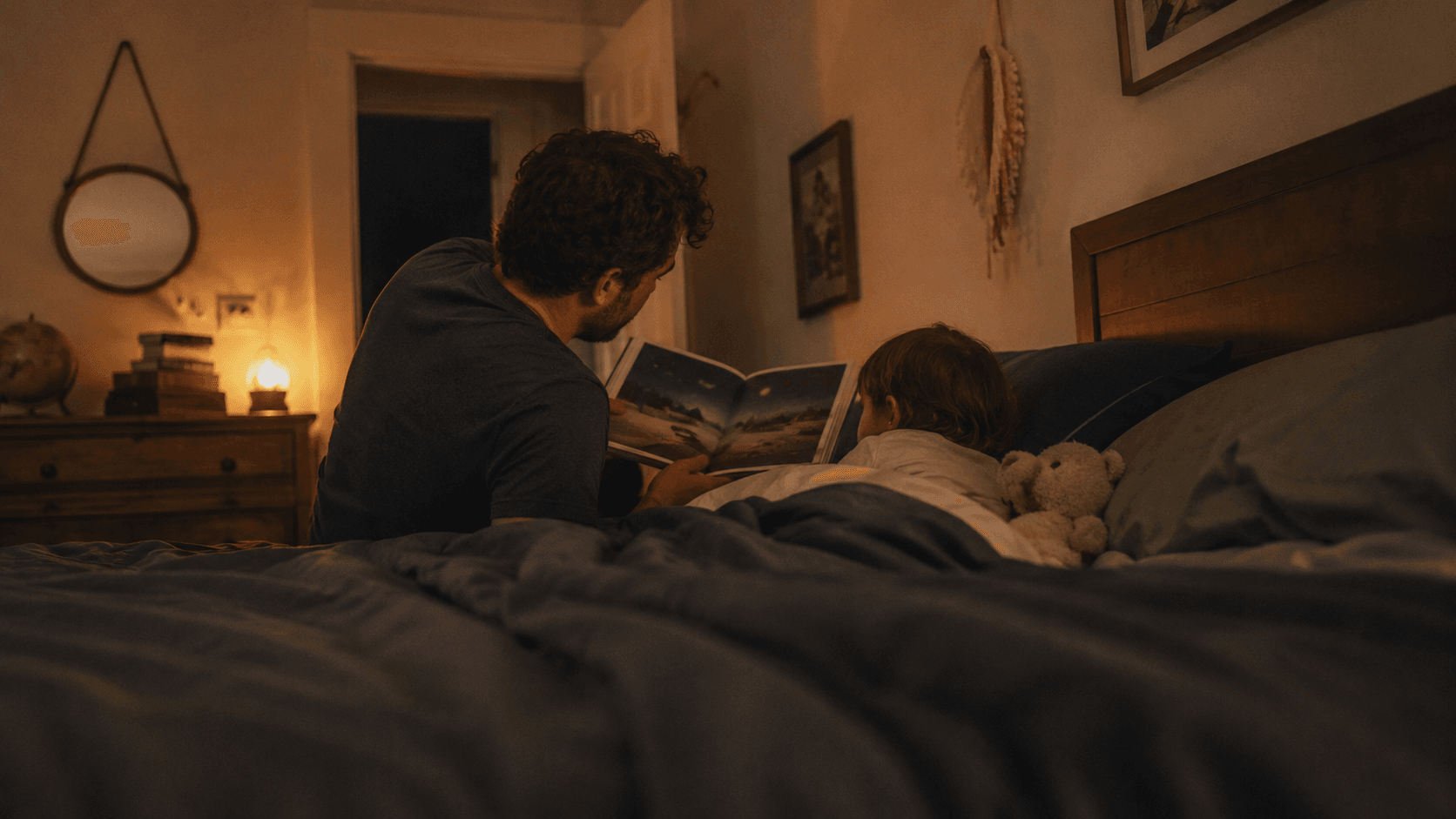 A father sitting on the edge of the bed reading a bedtime story to his son under a warm night lamp