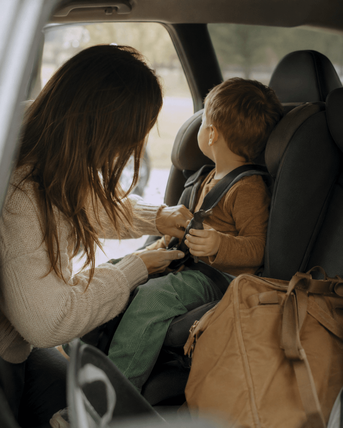 A mother buckles her son into his car seat harness during the school run
