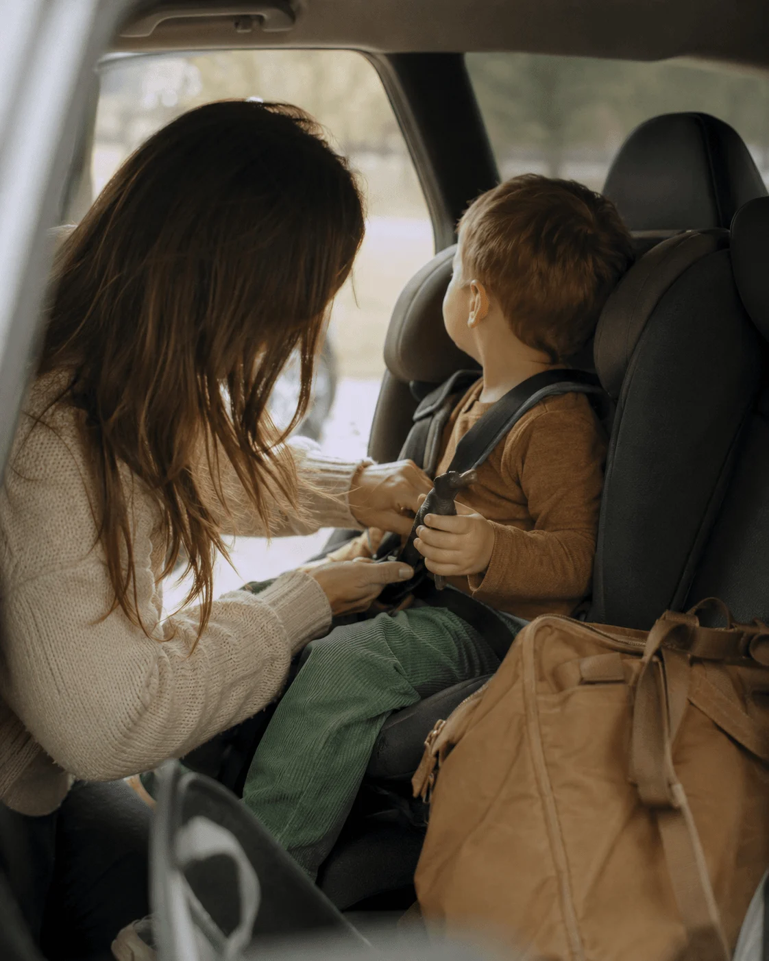 A mother buckles her son into his car seat harness during the school run