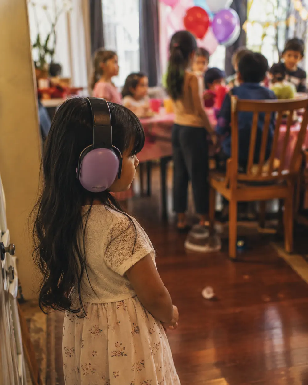 A girl in pink ear defenders standing at the edge of a busy children party