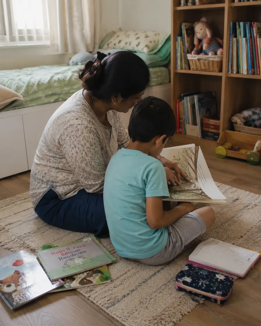 A mother and young son look at picture books together on a bedroom floor