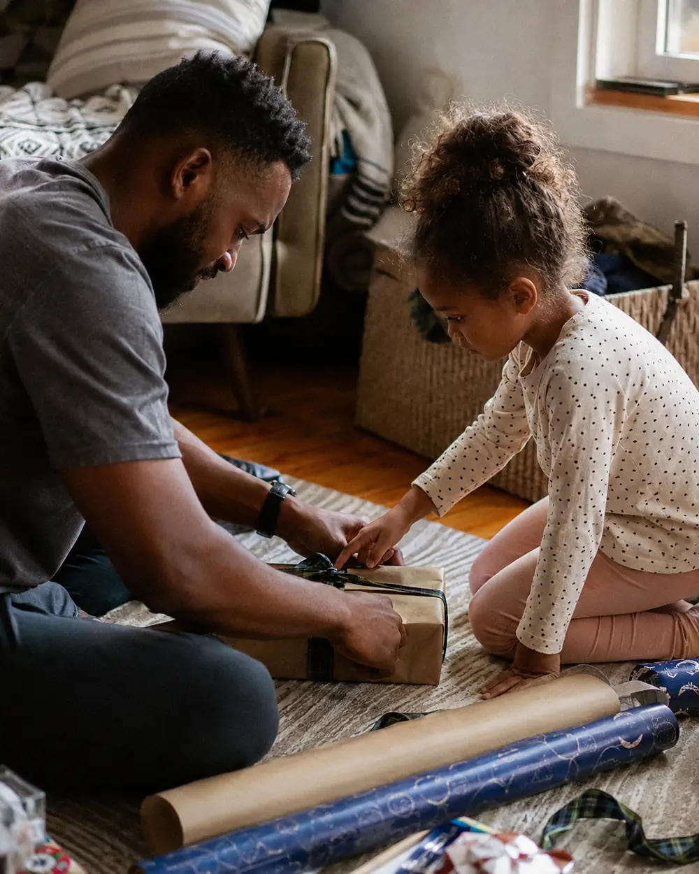 Two people taping sheets of wrapping paper together on a kitchen table late in the evening