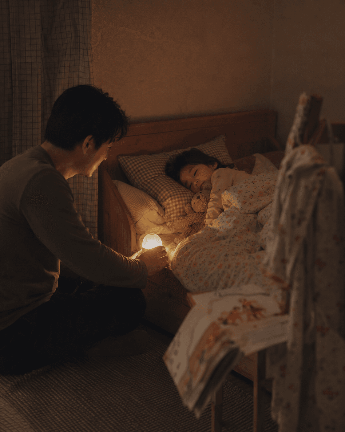 An Asian father checks on his daughter in bed by the warm glow of a round night light