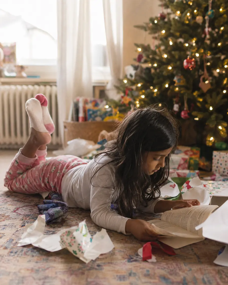 A child sits on the living room floor reading a newly unwrapped book