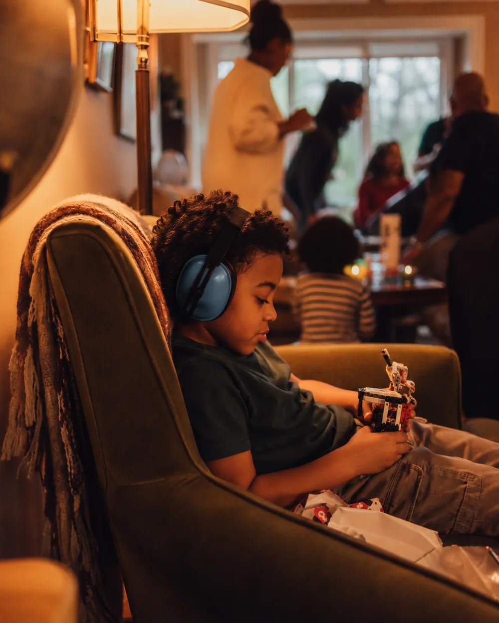A child sitting alone in a quiet corner wearing ear defenders while Christmas carries on behind them
