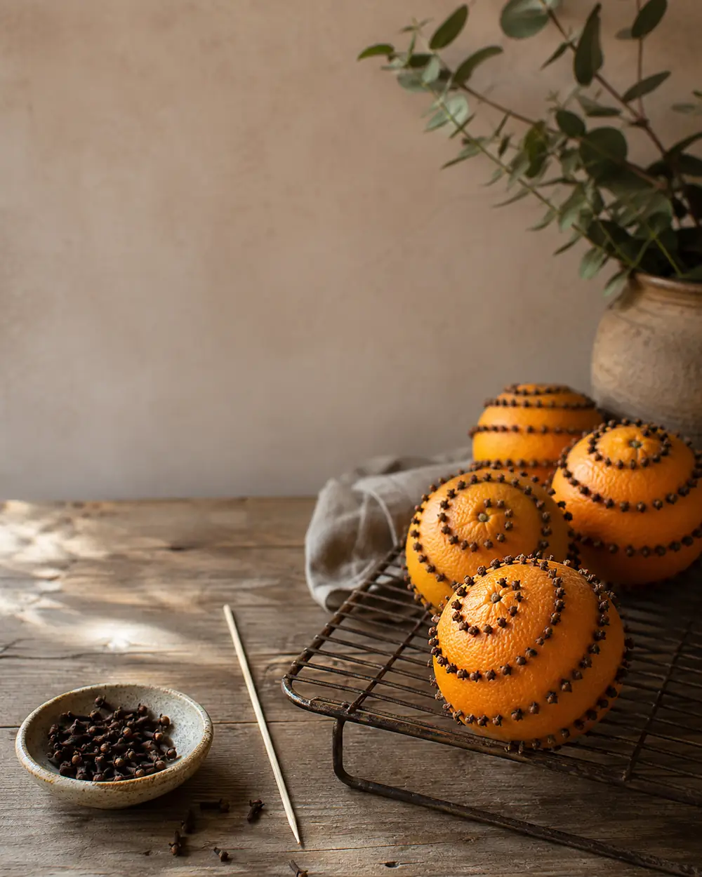An orange studded with whole cloves resting on a linen cloth in warm light