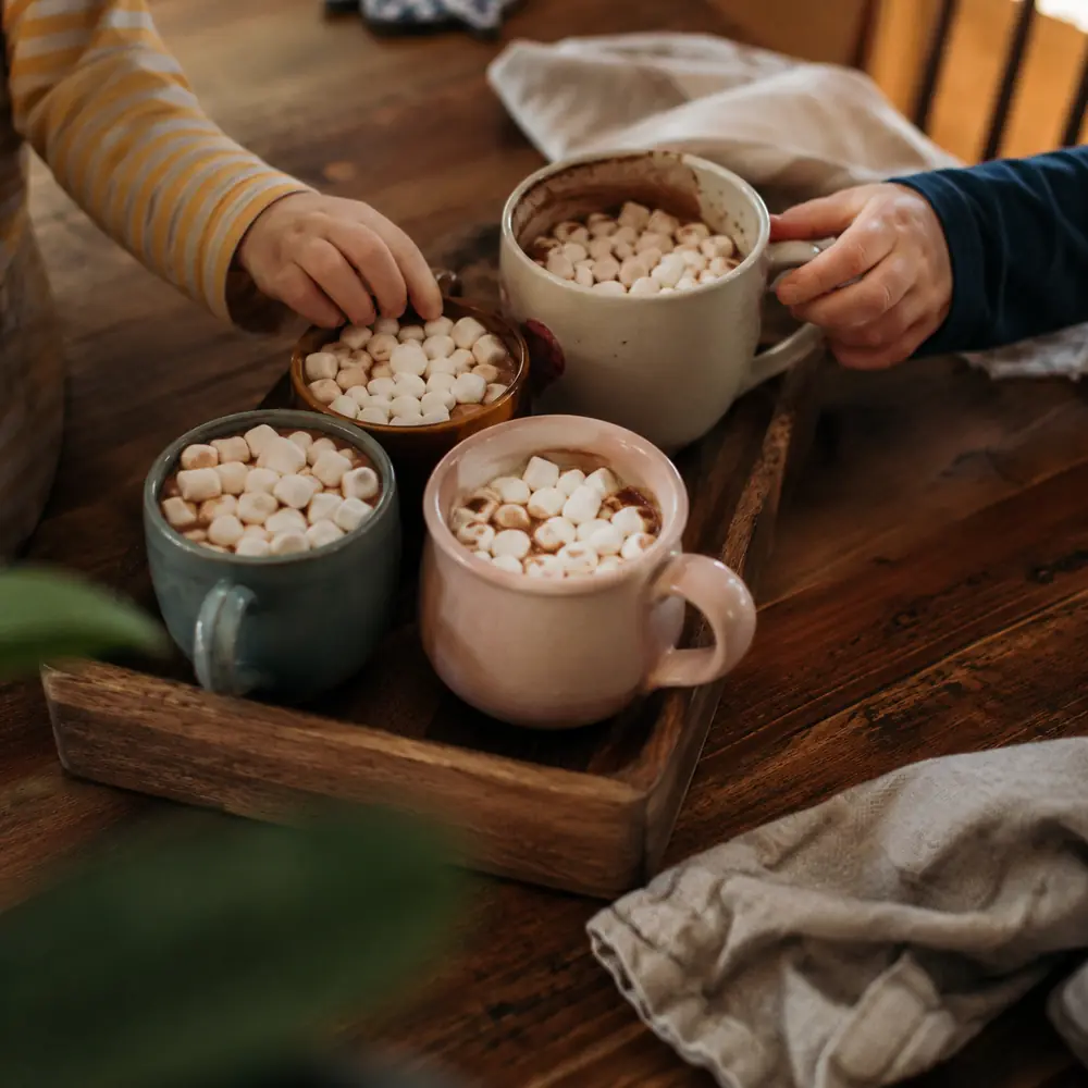 A tray of hot cocoa mugs topped with marshmallows on a kitchen counter