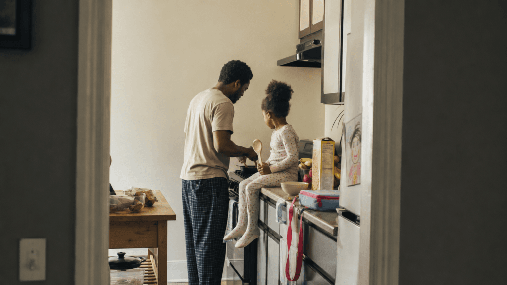 A father and his daughter in pyjamas cooking together at the stove in a warm morning kitchen