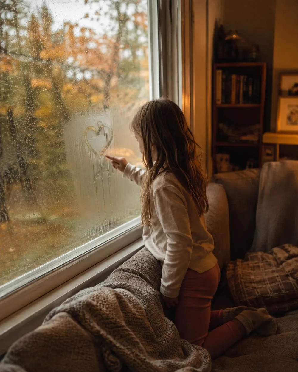 A child draws on paper beside a rain-streaked window on a grey autumn afternoon