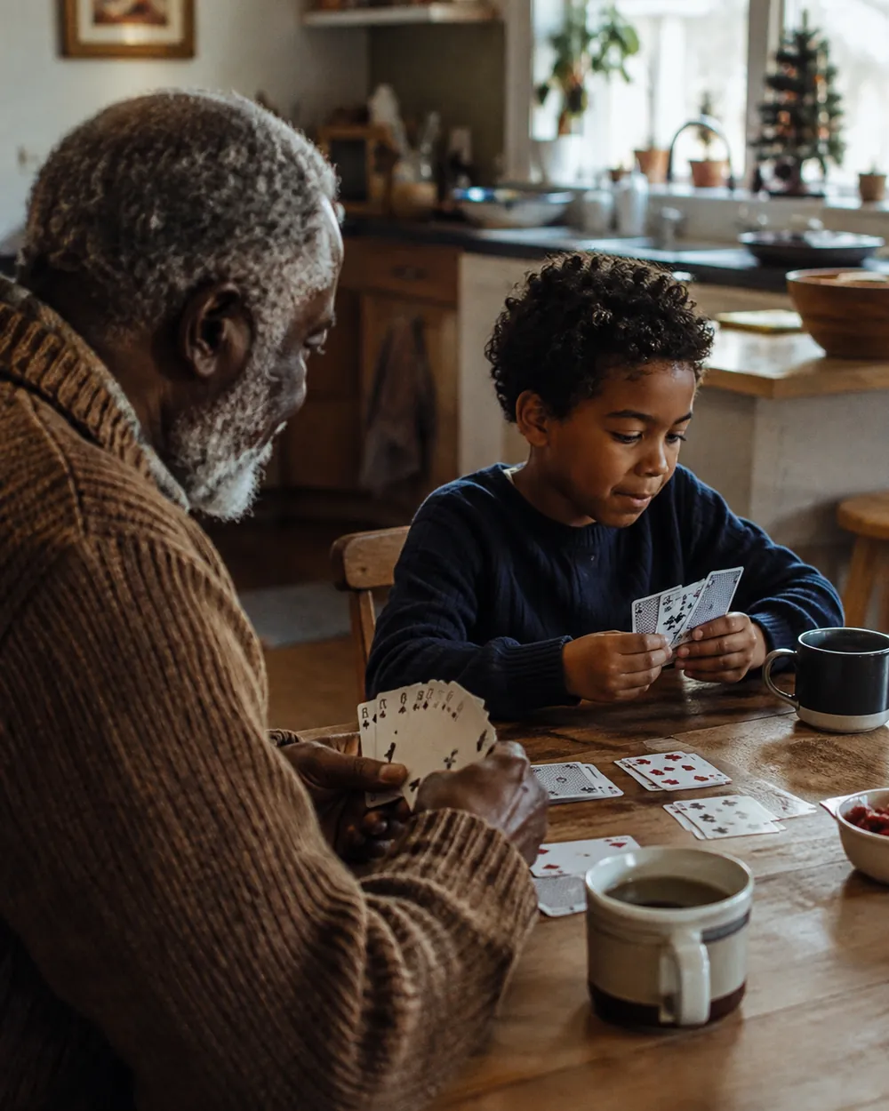 A grandparent and grandchild play a card game together at a table during a visit