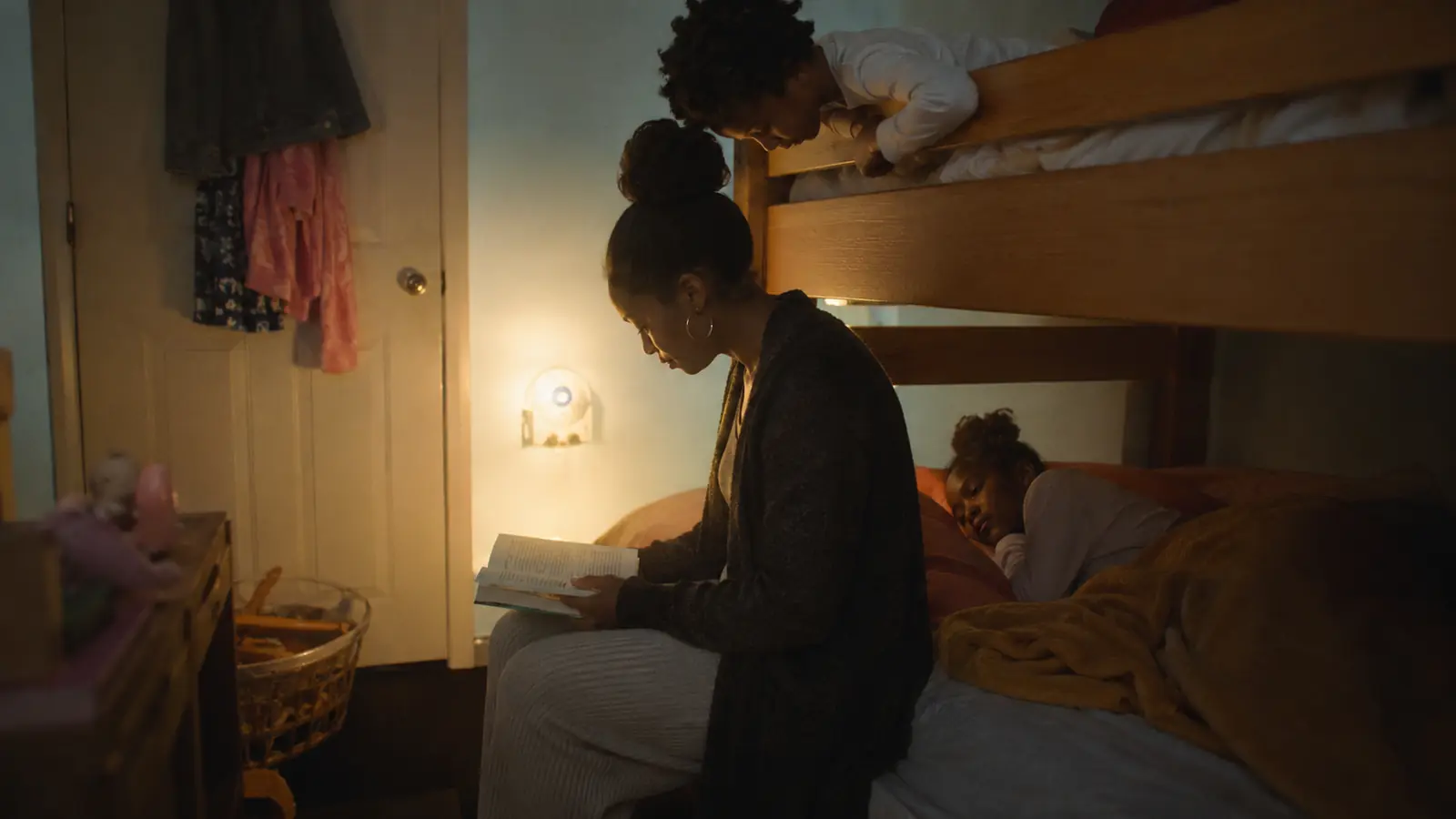 Two children listen to a story from their bunk beds in a shared bedroom at night