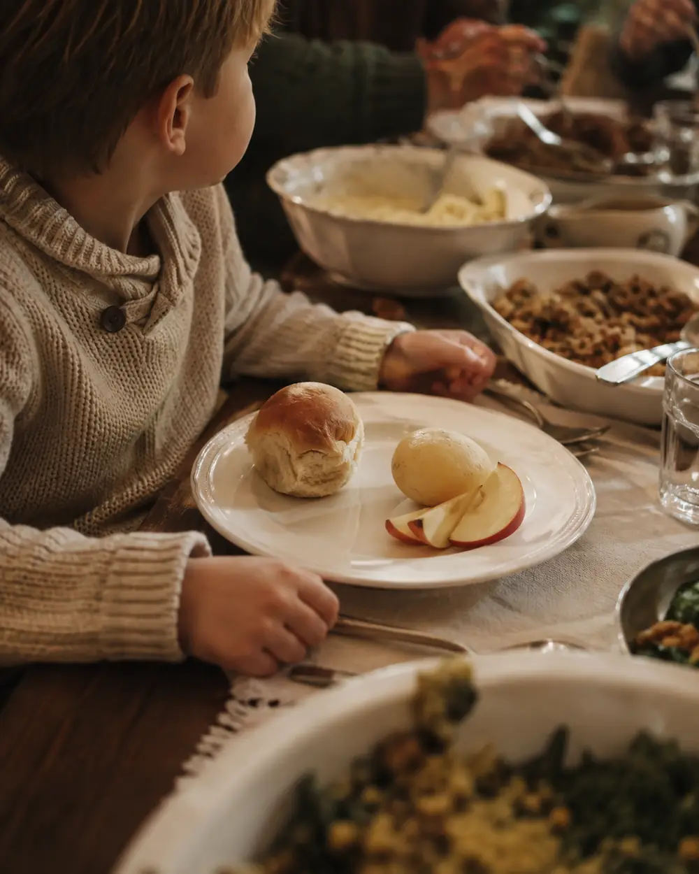 A child's plate at a holiday table holding bread and a small portion, the rest of the table spread behind it