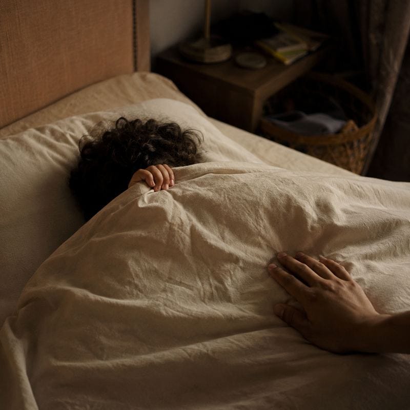 A child lies under a duvet in a quiet, dim bedroom