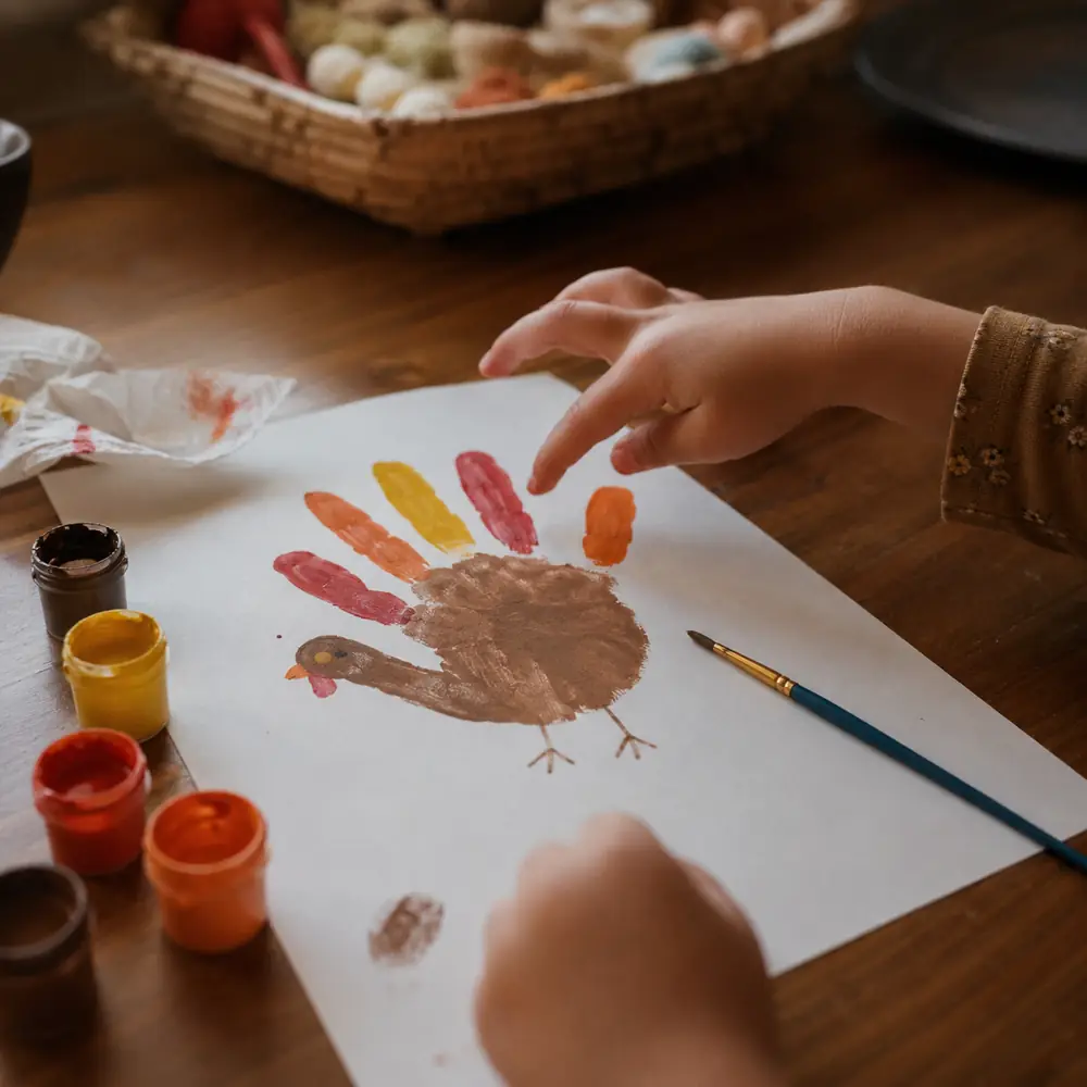 A child's hand traced on paper and coloured into a turkey, crayons scattered around it