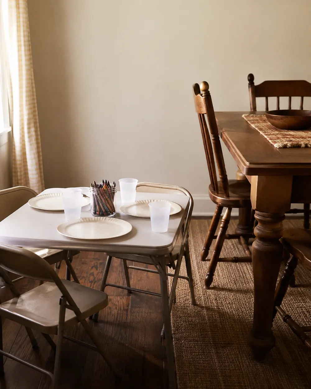 A small folding children's table set with paper plates and cups next to the grown-ups dining table