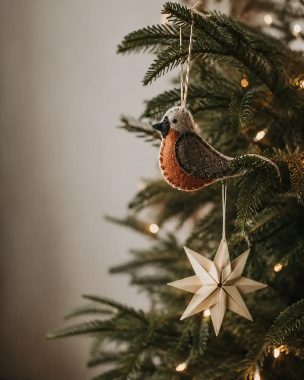 A felt robin ornament and a paper star hanging on the branches of a lit Christmas tree