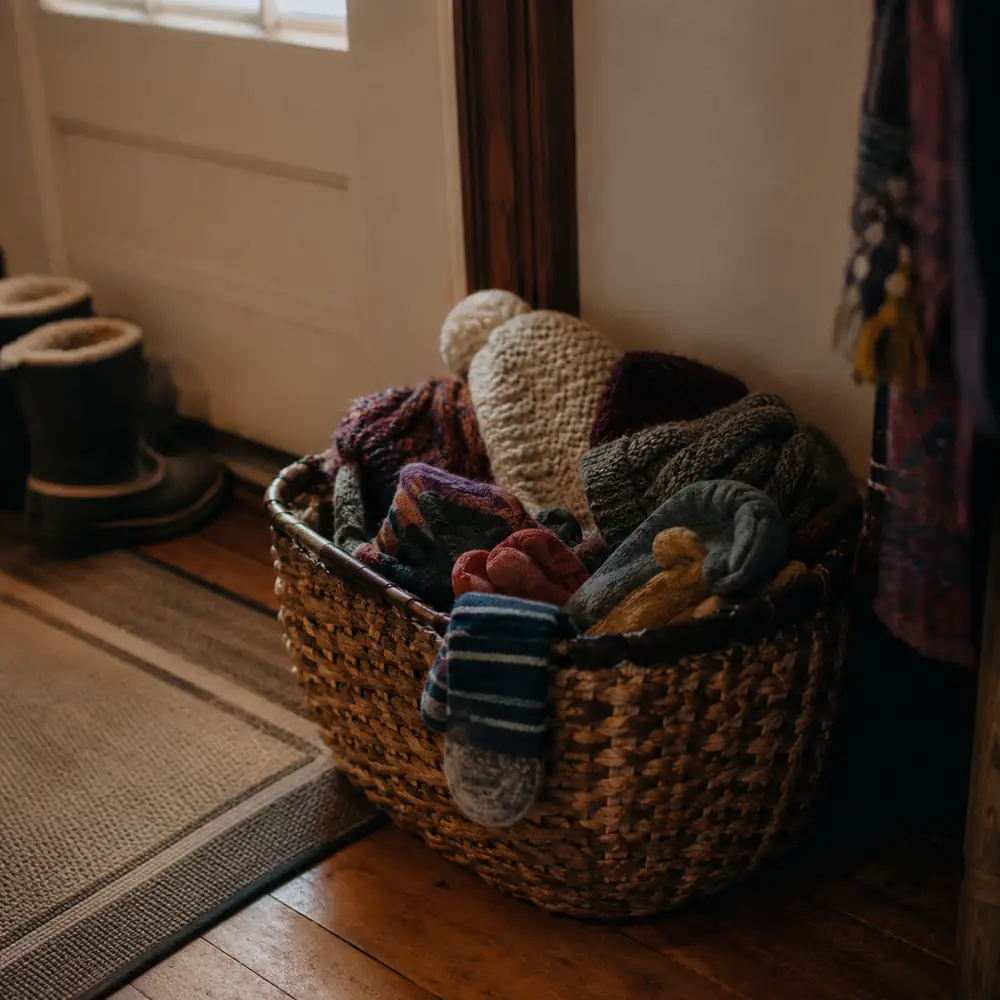 A woven basket of small mittens and hats sitting by a front door ready to go out