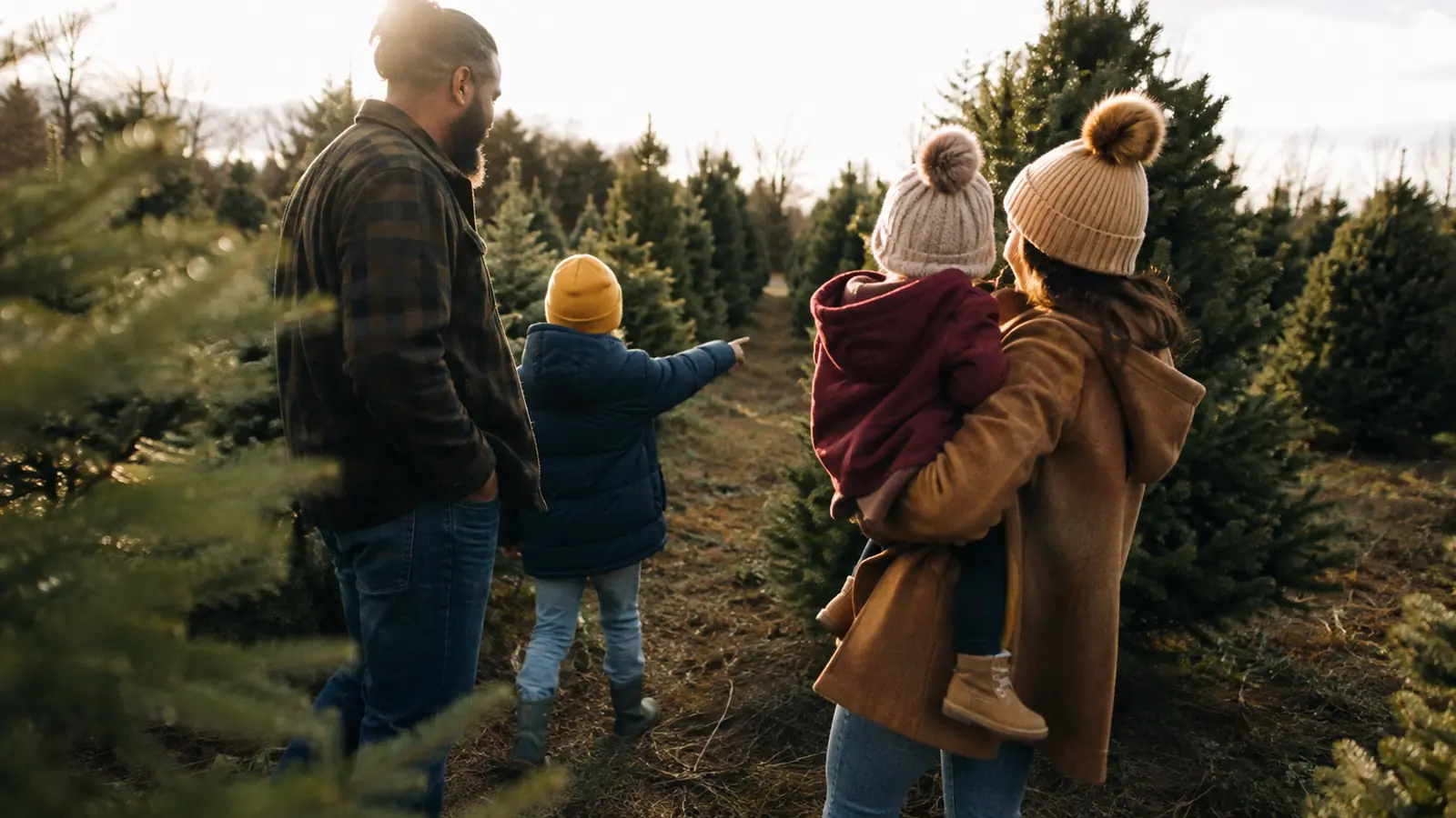 A parent and an older child walking rows of cut trees at a tree farm on a grey winter afternoon