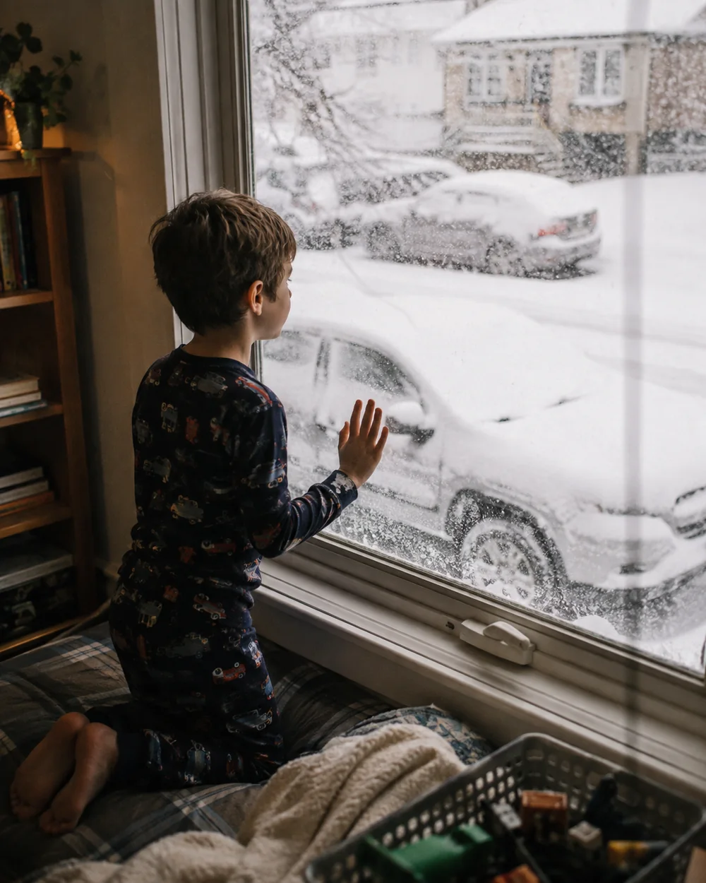 A child in pyjamas kneeling on a sofa and looking out of a frosted window in the morning