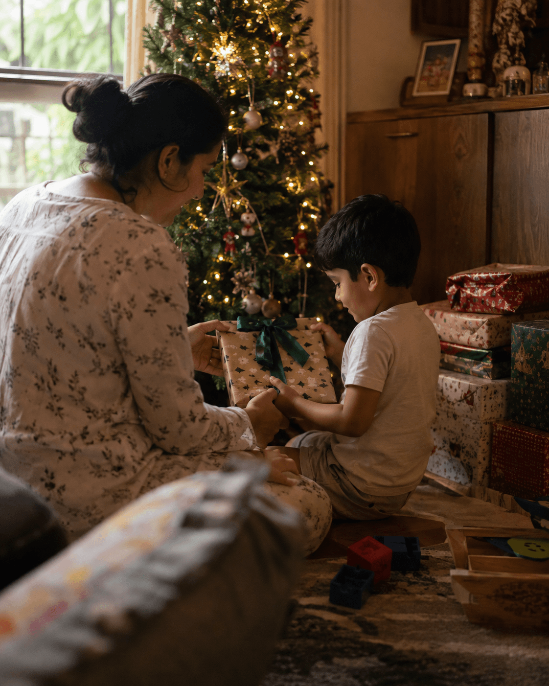 A young child carefully opening a single wrapped present while family members watch from the sofa