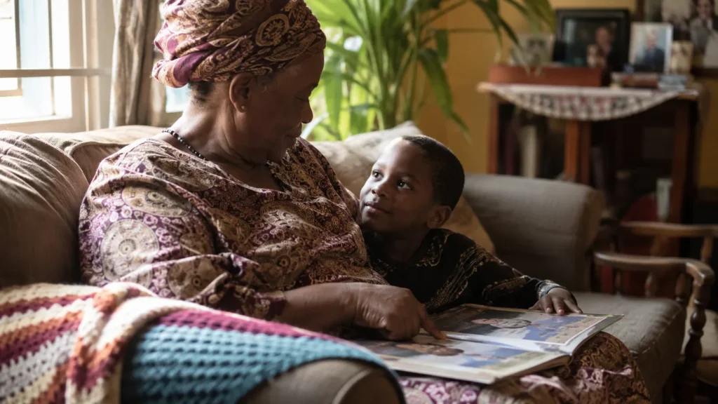A grandmother reading a picture book on a sofa with her grandson leaning against her