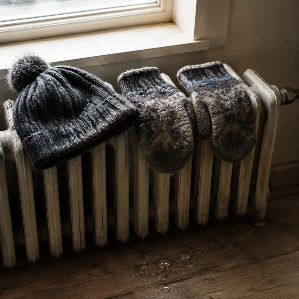 A knit hat and wool mittens drying on an old radiator