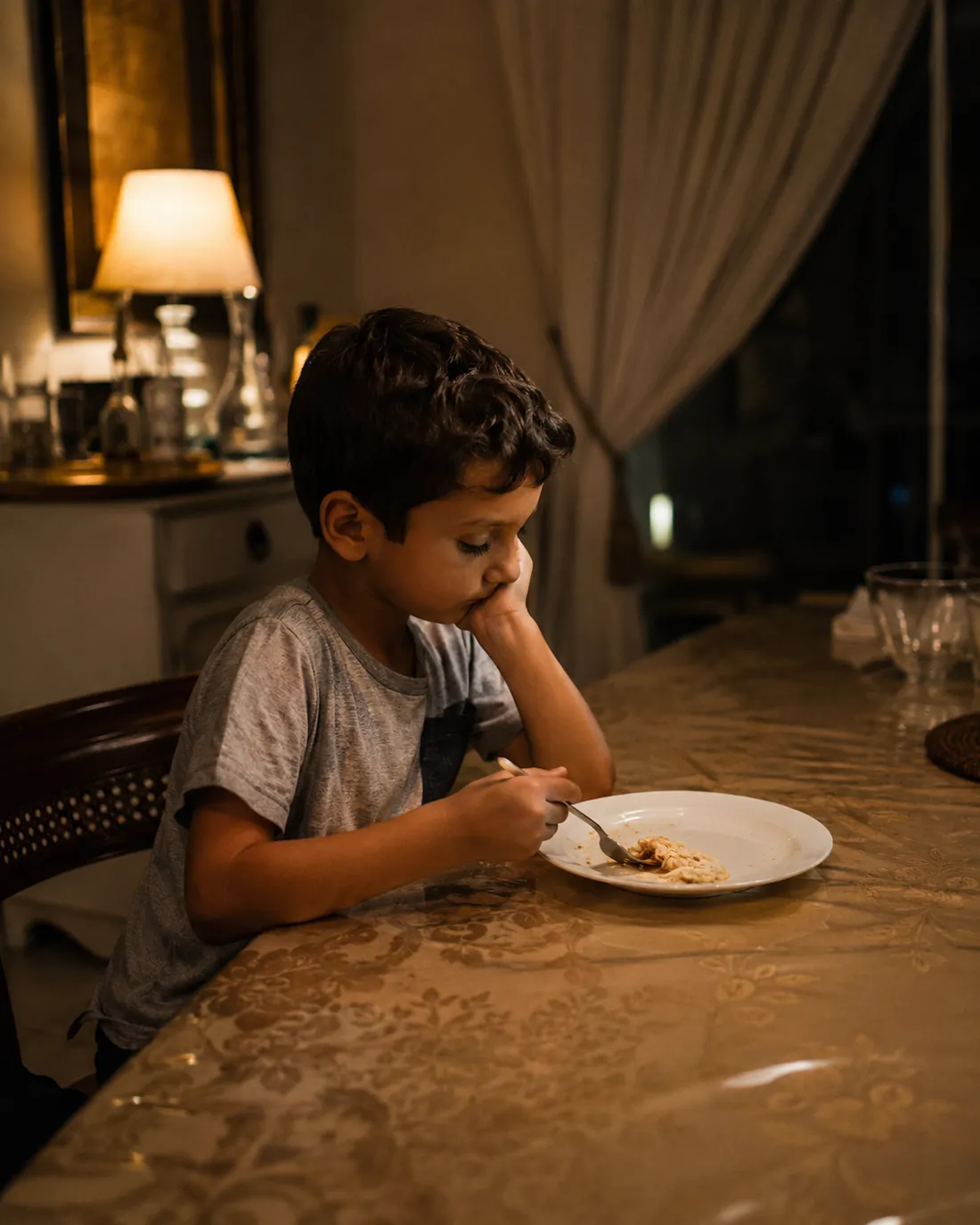A child sits at a table picking at a small plate of food