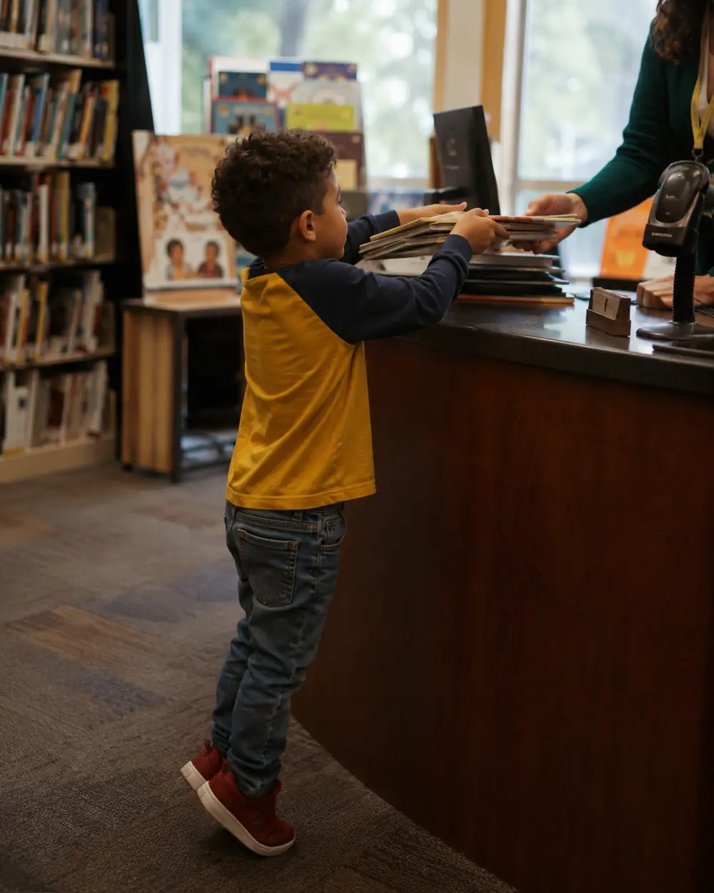 A child holding a library card at a library counter with a stack of books