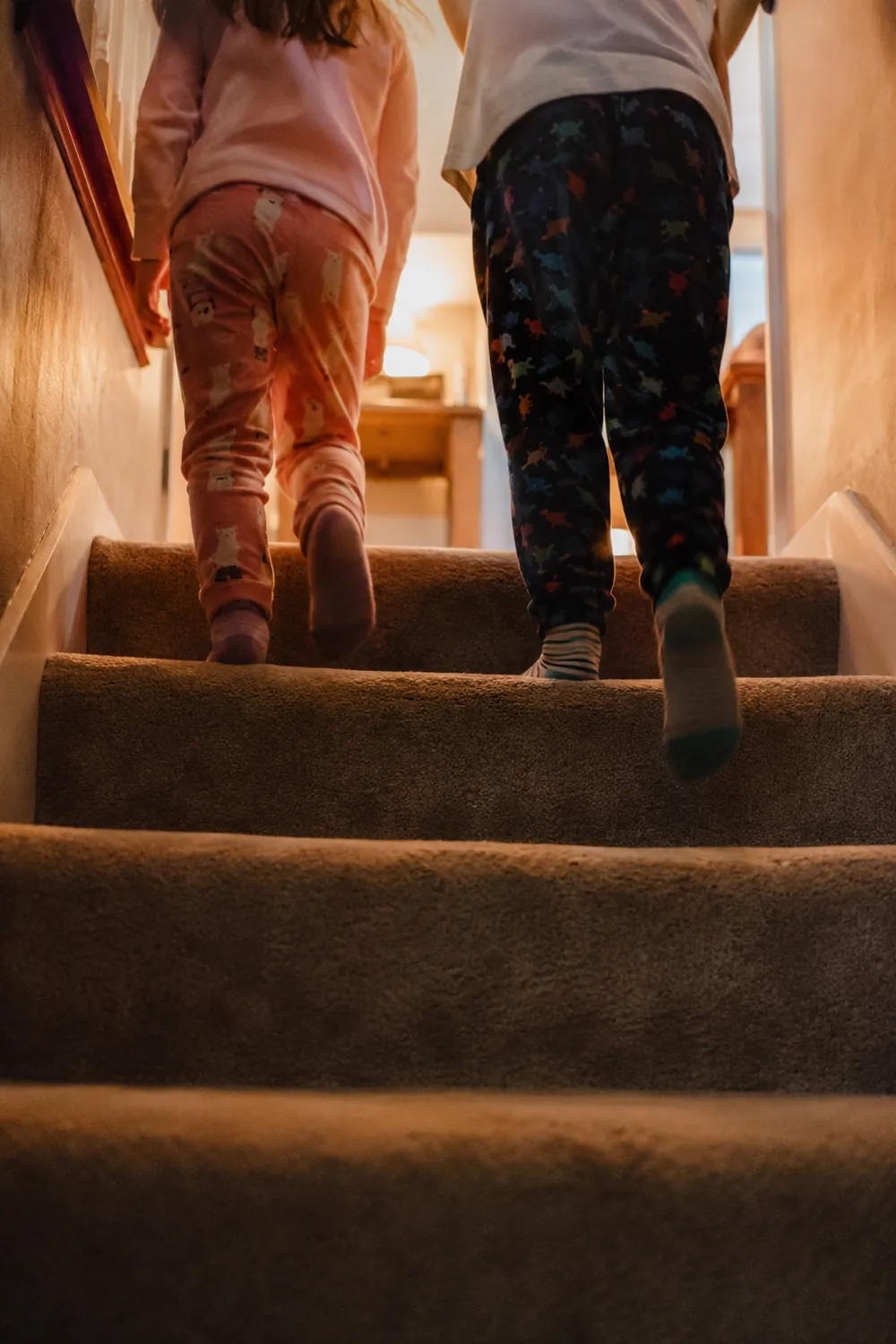 Two children in pajamas run up a carpeted staircase in socks on Christmas morning