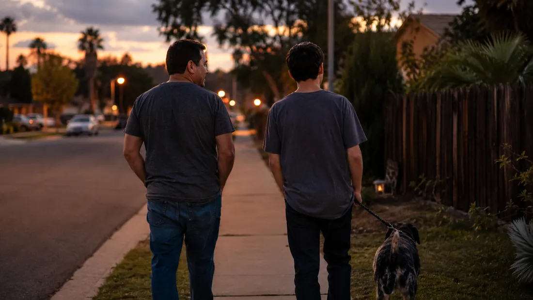 A dad and his teenage son walk side by side down a quiet street at dusk