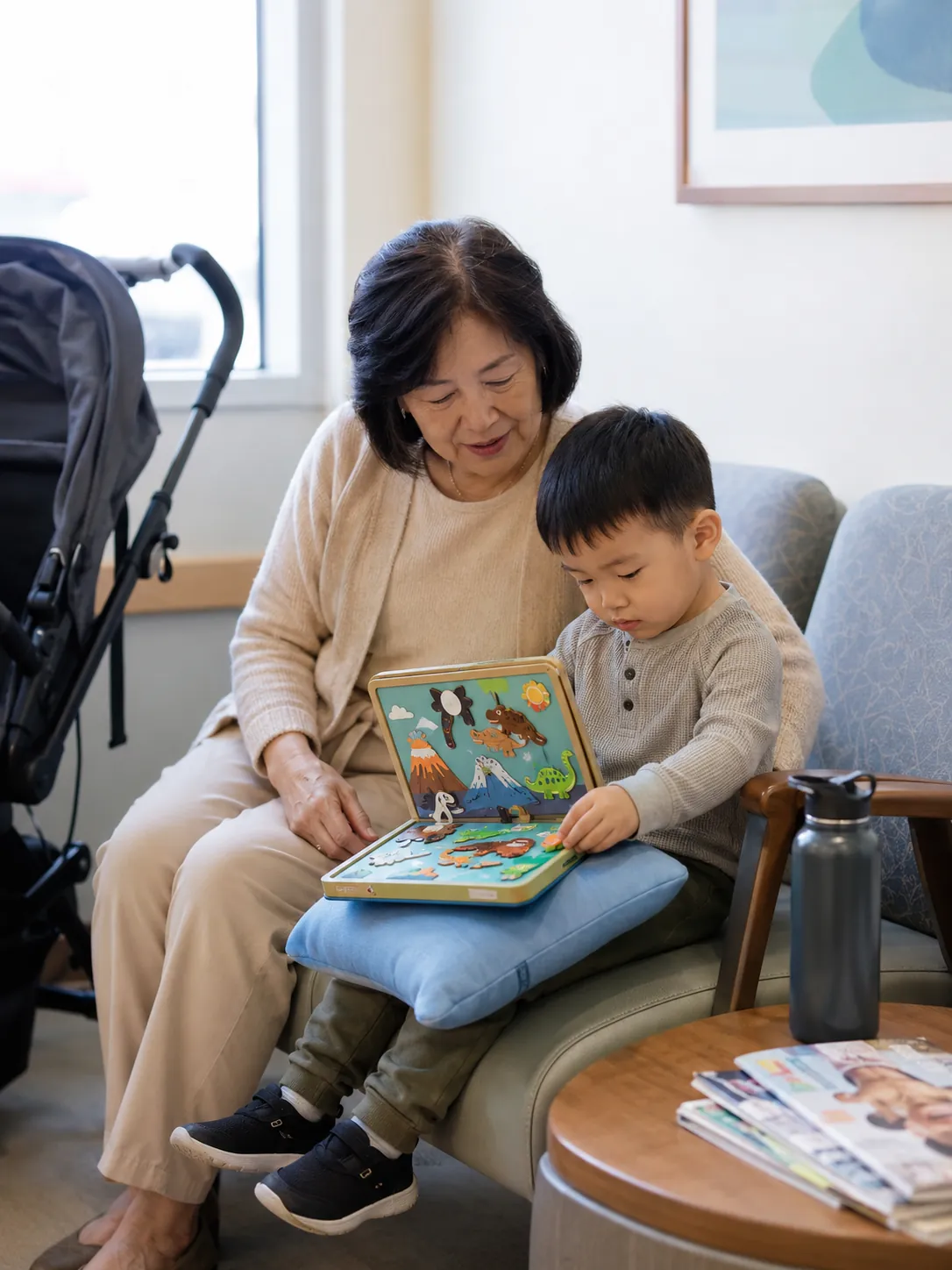A grandmother and toddler grandson play with a puzzle book in a pediatrician's waiting room