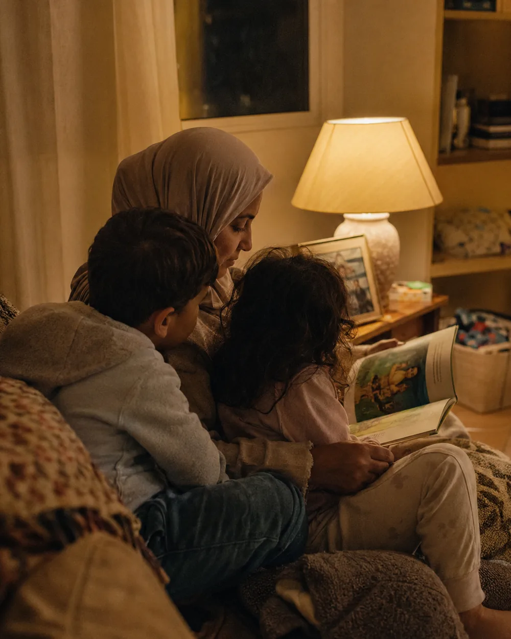A child listening to a story under a lamp in a room that is already dark outside