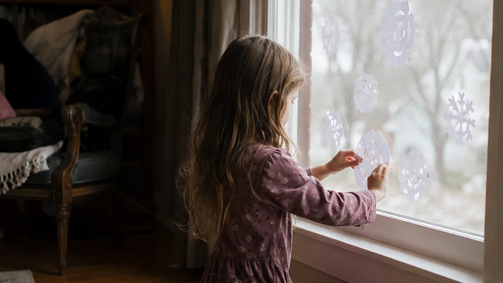 Paper snowflakes taped to a window with the dark evening outside