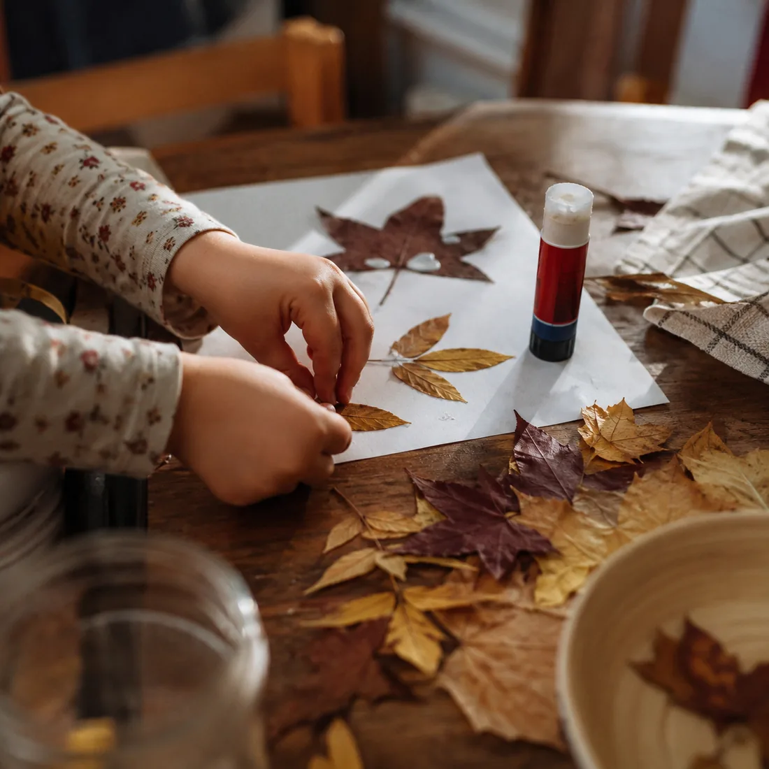 Autumn leaves and a glue stick spread across a table mid craft