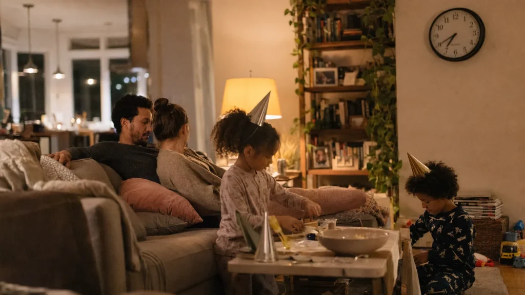 A family gathered in a living room in the evening with a clock on the wall behind them