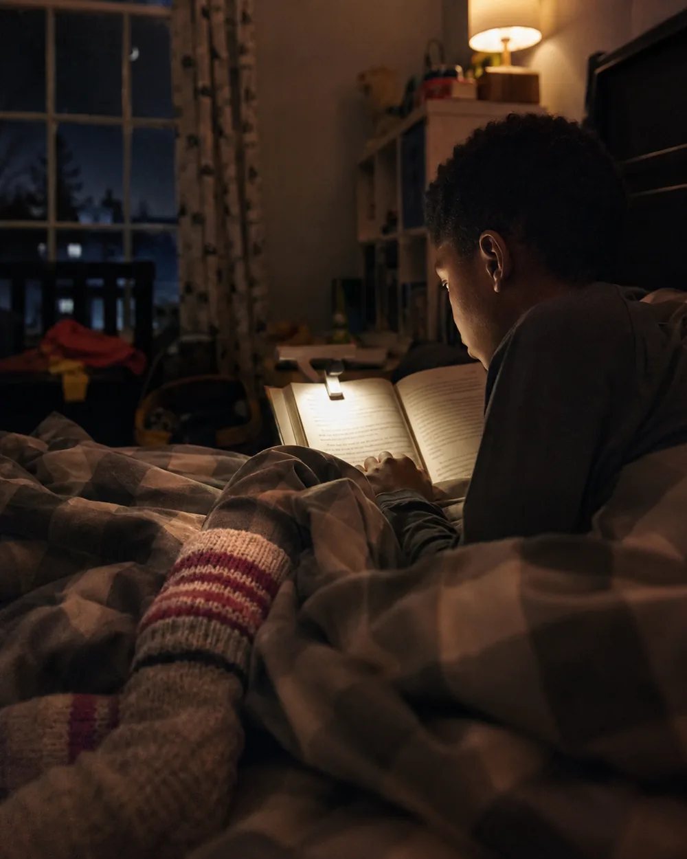 A child in warm socks reading in bed under a soft light