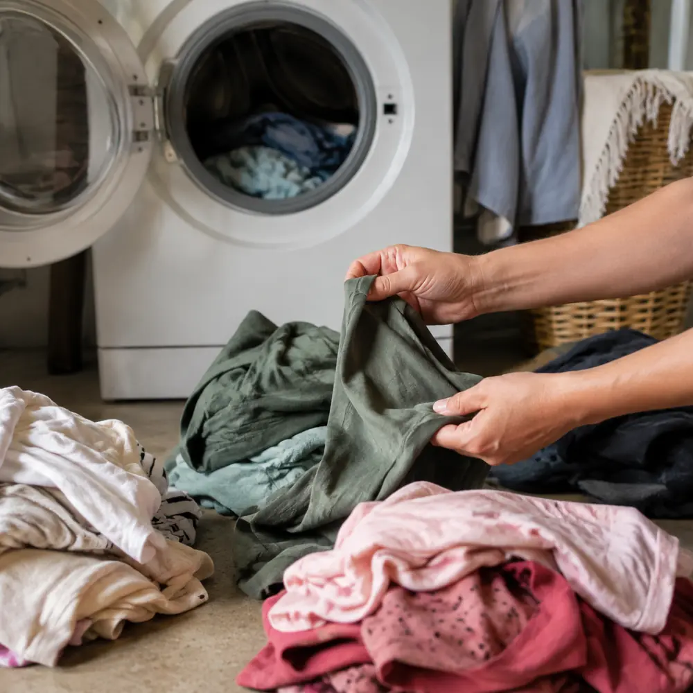 Hands sorting piles of laundry in front of a washing machine