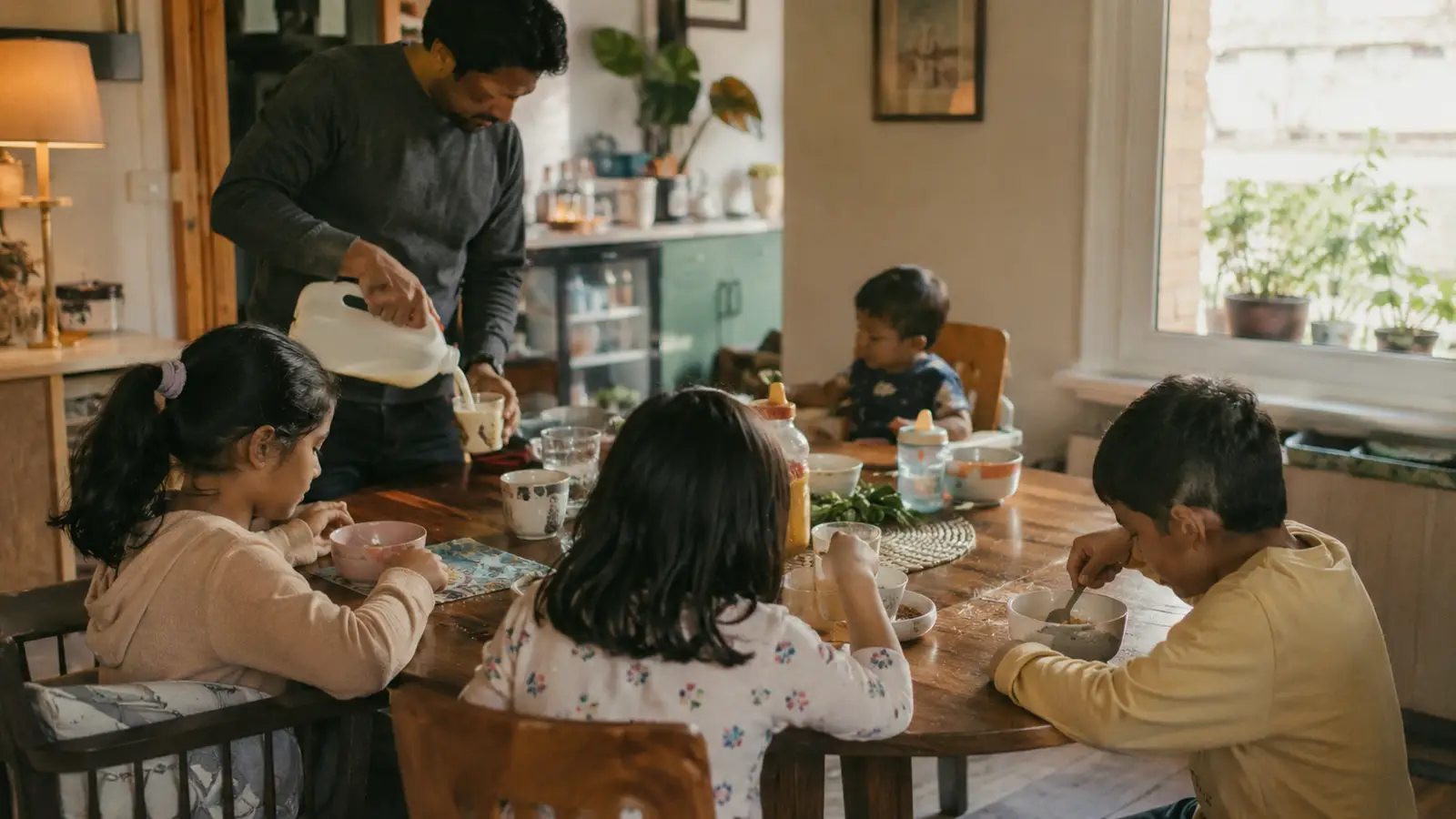 A South Asian family sit around a crowded table mid-meal with dishes and cups everywhere
