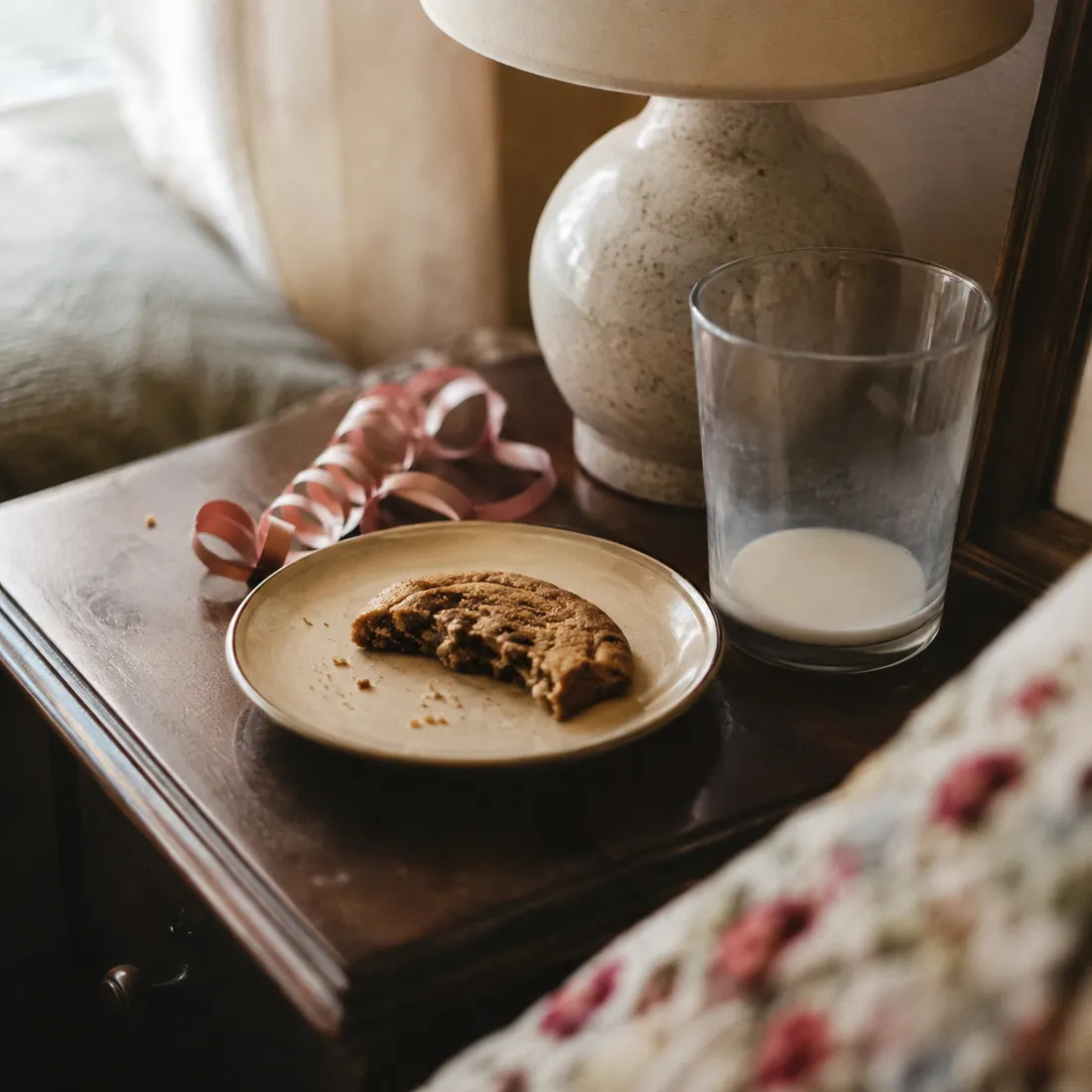 A plate of cookie crumbs and a half-empty glass of milk on a side table